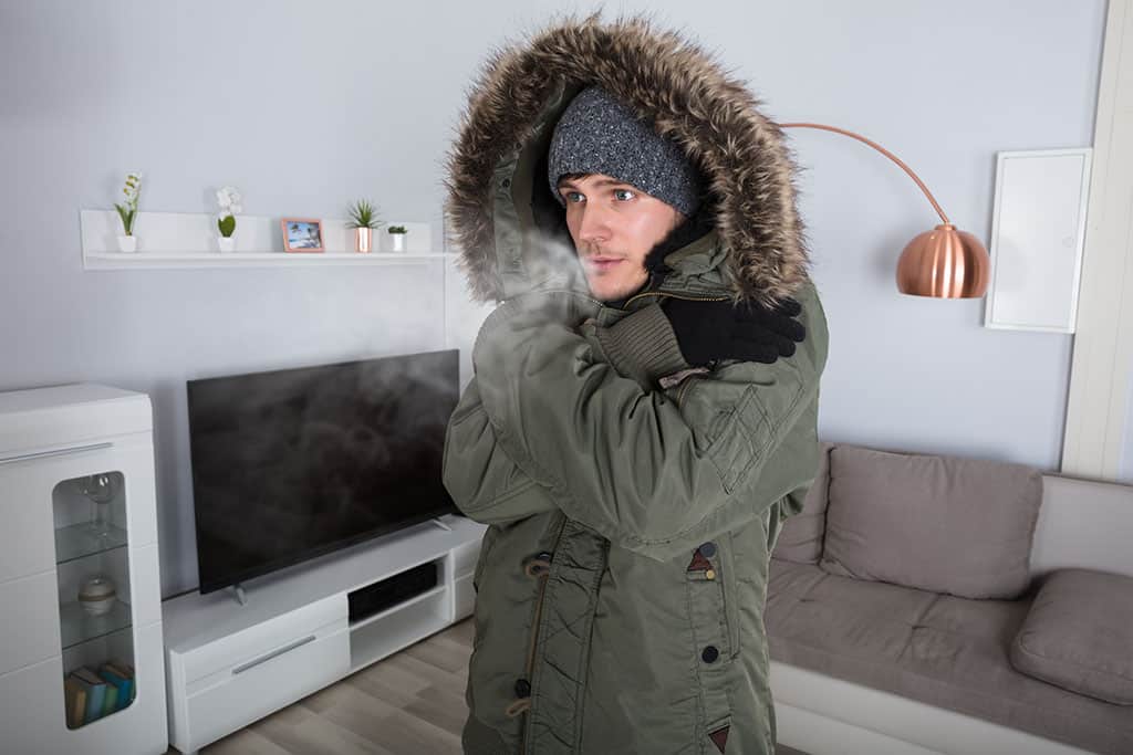 man wearing jacket inside living room because furnace is broken