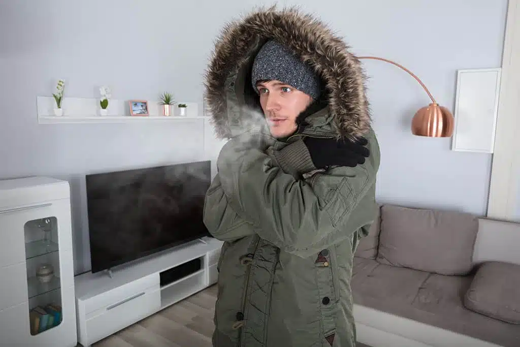 man wearing winter coat inside because heater is broken