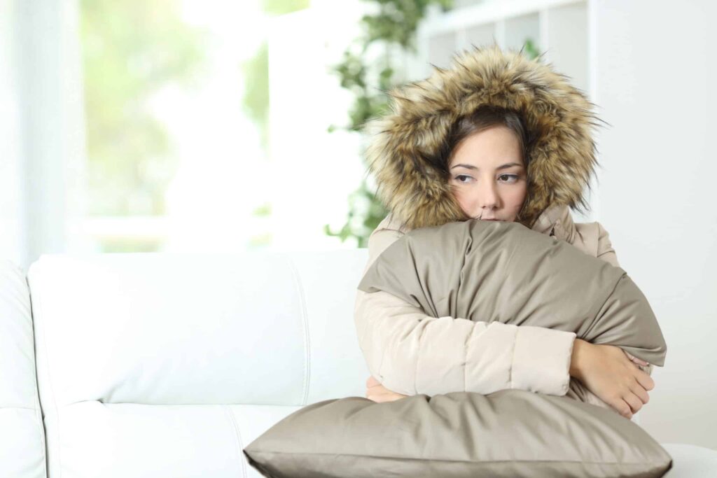 Woman warmly clothed in a cold home sitting on a couch