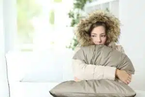 Woman warmly clothed in a cold home sitting on a couch