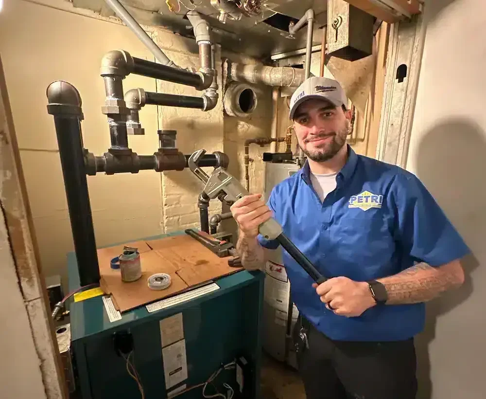 Petri technician holding a pipe wrench and smiling while working at a residential job site in Brooklyn, NY.